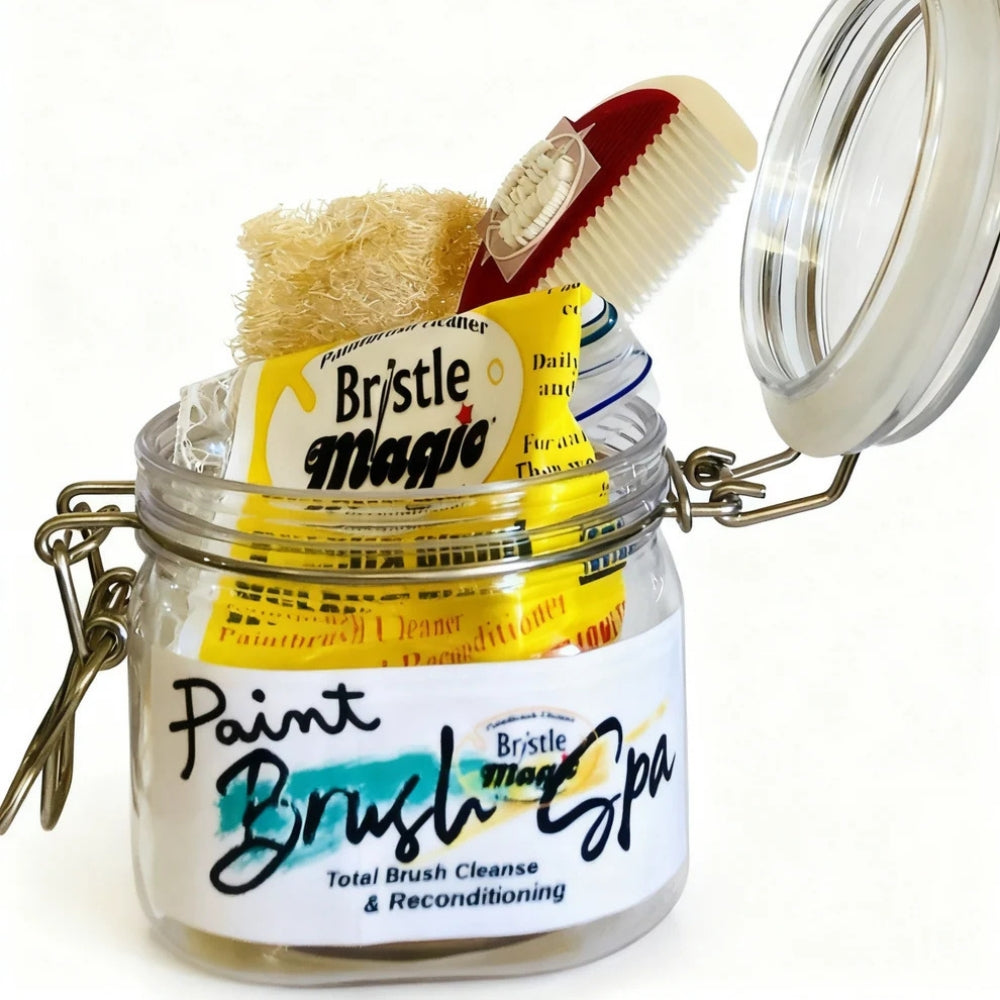 A glass jar labeled 'Paint Brush Spa' with an open hinged lid, containing packaged bristle brushes and a natural scrubber. The visible product packaging includes a yellow packet reading 'Bristle Magic'.